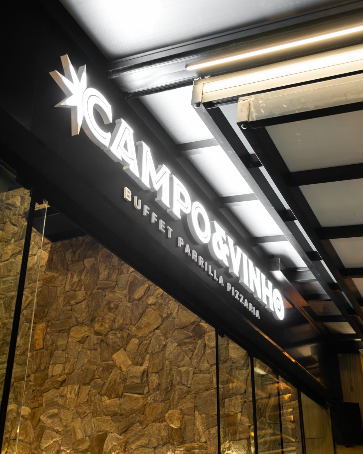 Letreiro iluminado do Campo & Vinho, buffet, parrilla e pizzaria, na fachada de pedra