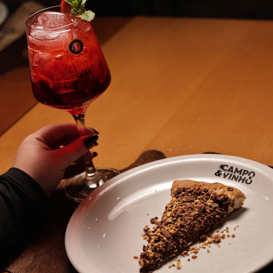 Fatia de pizza doce de chocolate no prato do Campo & Vinho, ao lado de um drink vermelho com morango